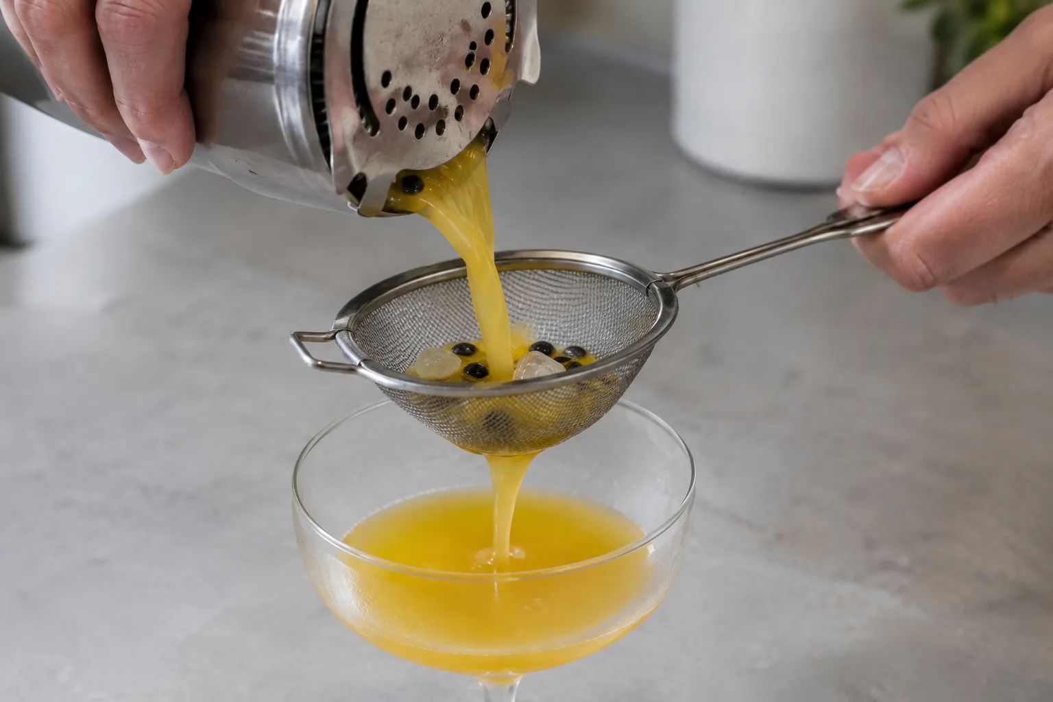 A cocktail passes through a shaker strainer and fine-mesh sieve, leaving passion fruit seeds behind.