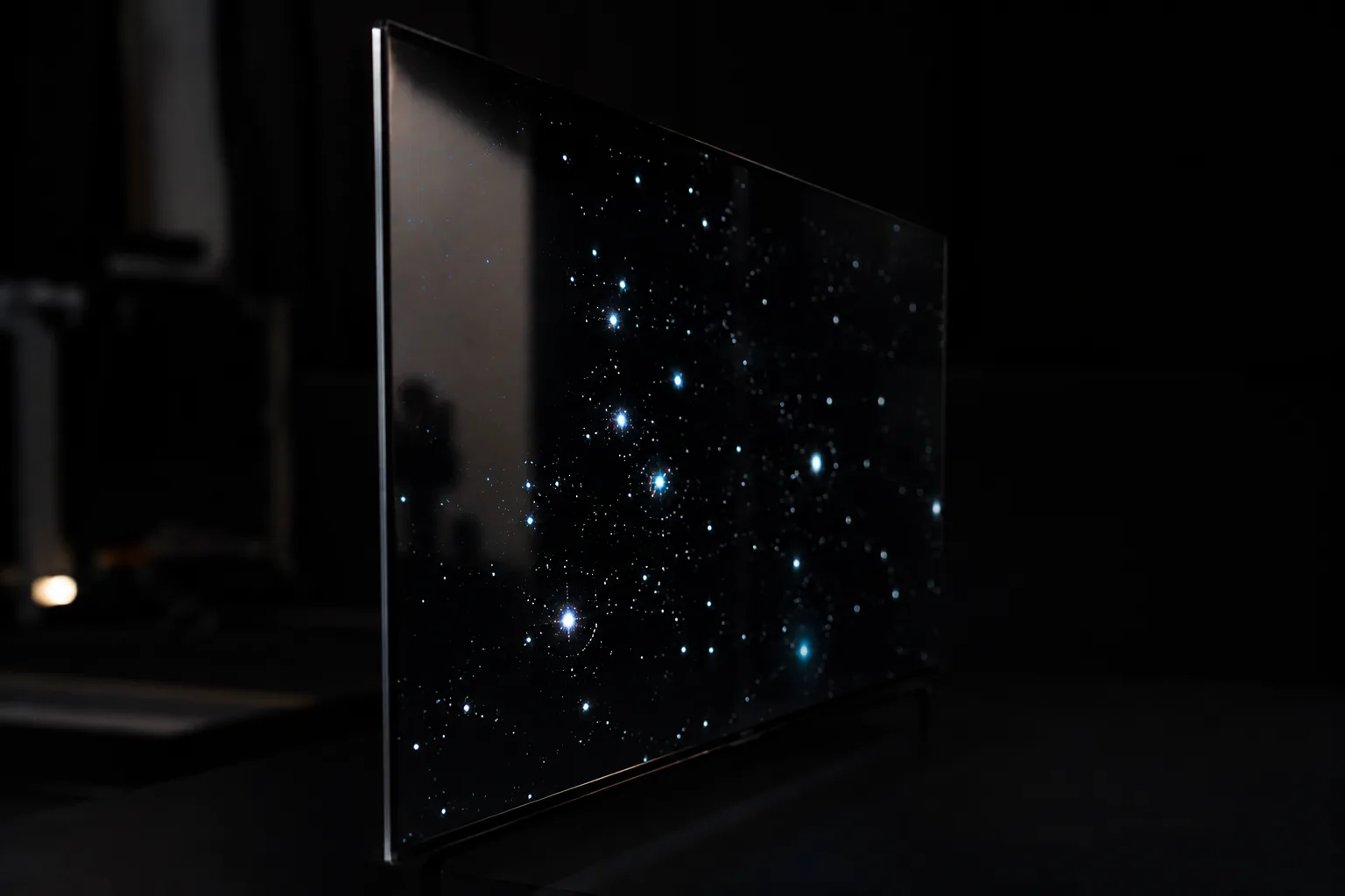 Bright stars shine on a thin OLED screen whose black areas blend into the dark room.